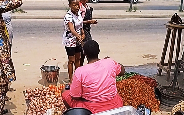 Tax agent (black short) collecting tax from the tomato seller at 8 Miles market.