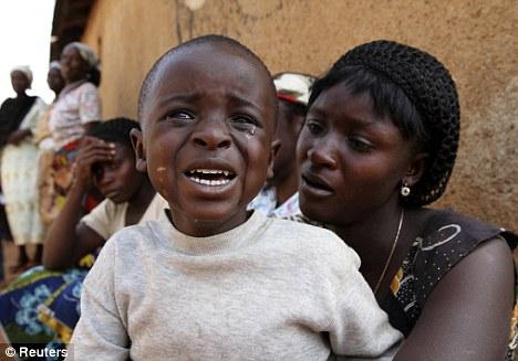 A boy sitting with his mother cries during a funeral for people killed in religious attacks